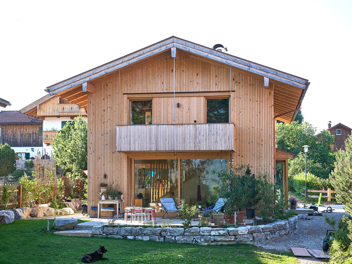 Ein zweistöckiges Haus mit Holzfassade, links ist eine Garage angebaut.